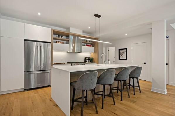A modern kitchen with a central island, stainless steel appliances, and bar stools.