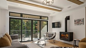 Ein modernes Wohnzimmer mit Sofa, Sessel, Kamin und einem Balkon mit Glastüren.
