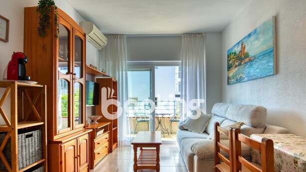 A living room with a sofa, wooden cabinets, a TV, and a painting on the wall. - Apartment in the center of Platja d'Aro with pool and A/C (Platja d'Aro)