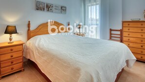 A bedroom with a wooden bed, a nightstand with a lamp, a dresser, and a ceiling fan. - Apartment in the center of Platja d'Aro with pool and A/C (Platja d'Aro)