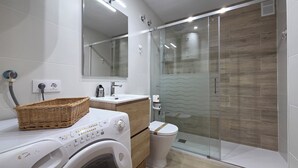 A modern bathroom with a washing machine, a sink, a toilet, and a glass shower enclosure. - Apartment in the center of Platja d'Aro with pool and A/C (Platja d'Aro)