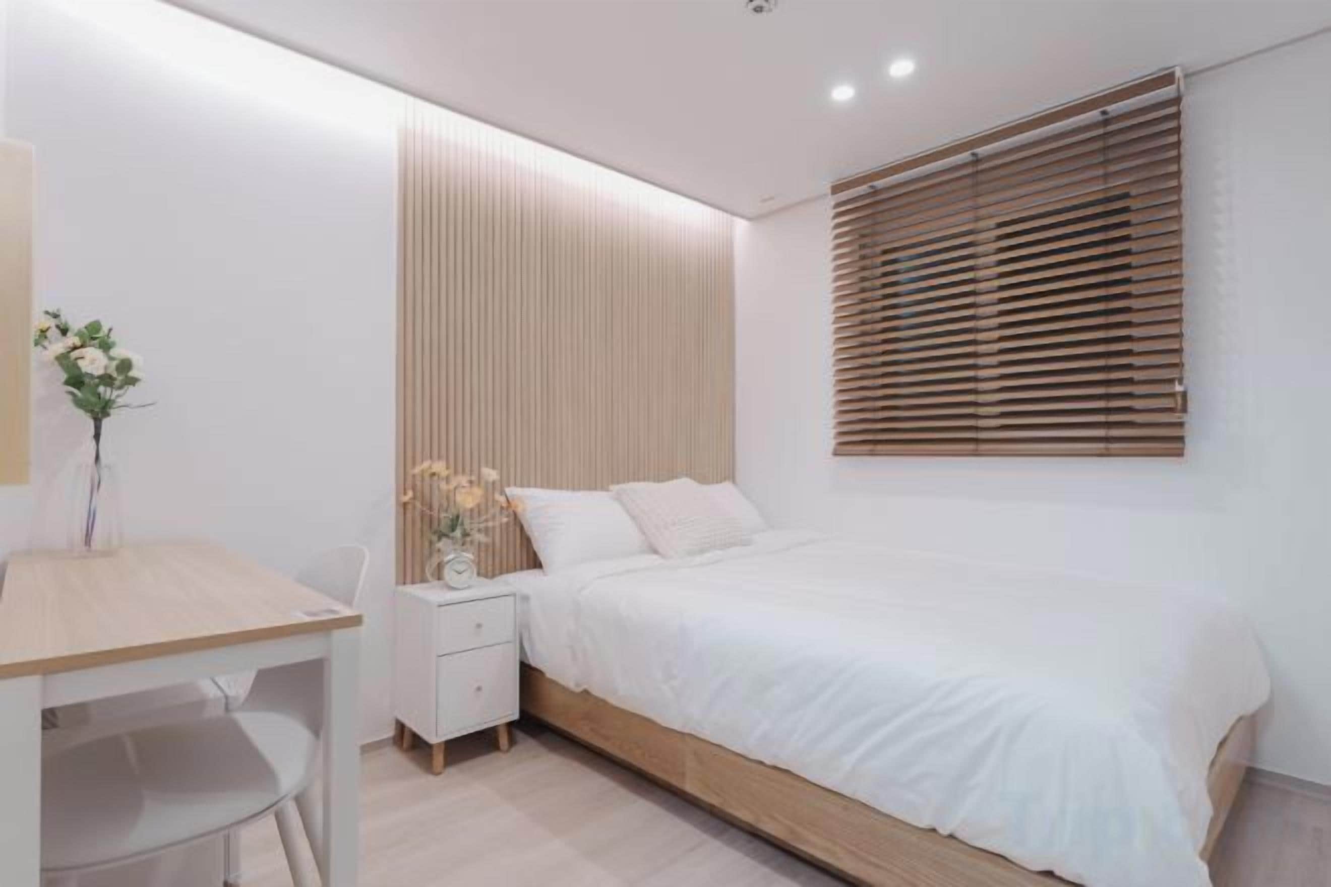 Een slaapkamer met een bed, nachtkastje en een bureau met stoel.