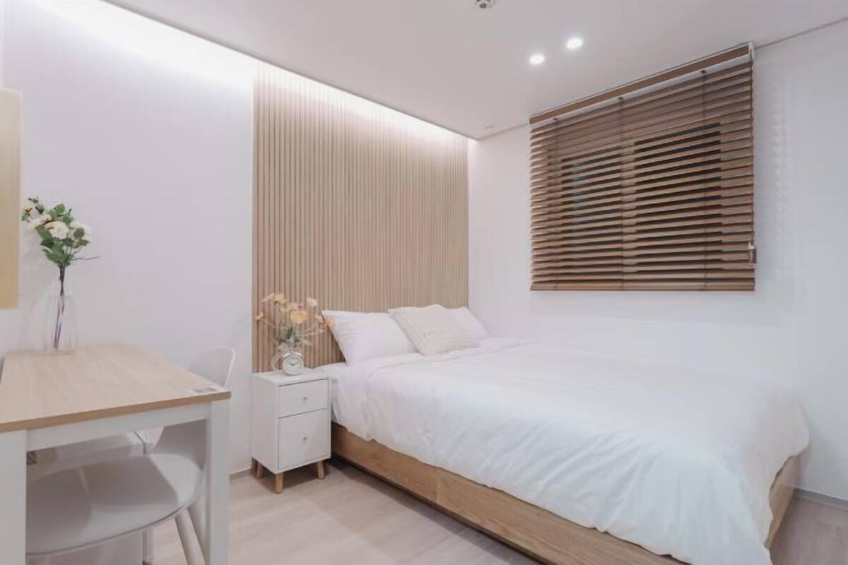 A bedroom with a bed, bedside table, and a window with blinds.