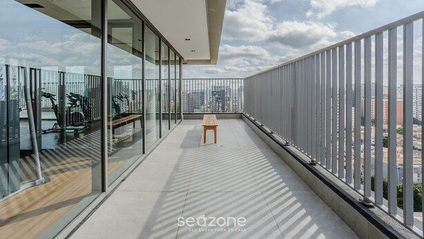 Un balcon moderne avec des parois en verre, un banc en bois et une vue sur le paysage urbain.