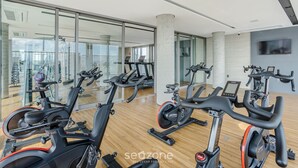 Une salle de sport équipée de plusieurs vélos d’exercice, dotée de grandes fenêtres et d’un plancher en bois.