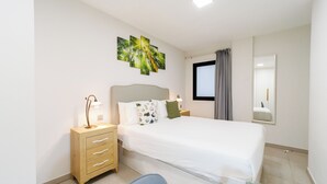 Habitación de hotel con cama, mesitas de noche, escritorio, silla, ventana con cortinas y espejo en la pared.