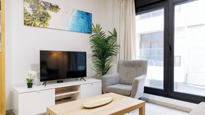 Una sala de estar moderna con un televisor de pantalla plana, un sillón gris, una mesa de centro de madera y un ventanal con vistas al exterior.