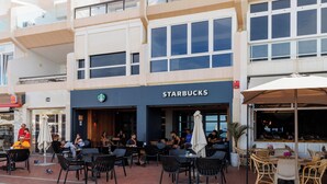 Una Starbucks con terraza al aire libre, suelo de ladrillo y un edificio de dos pisos con balcones.