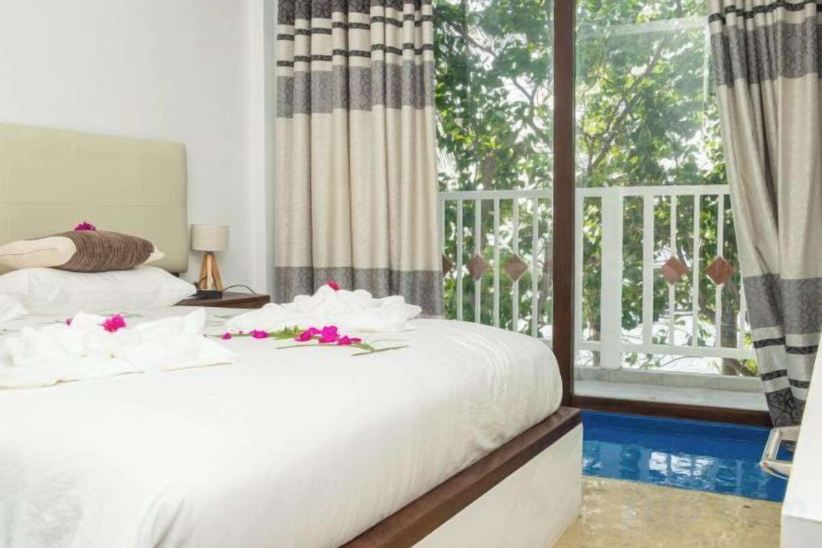 A hotel room with a bed, a nightstand, a lamp, a view of a balcony, and a pool.