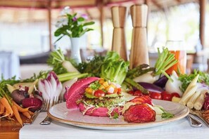 A plate with a layered dish, surrounded by various vegetables and herbs. - Heron Beach Hotel Dhiffushi (Dhiffushi)