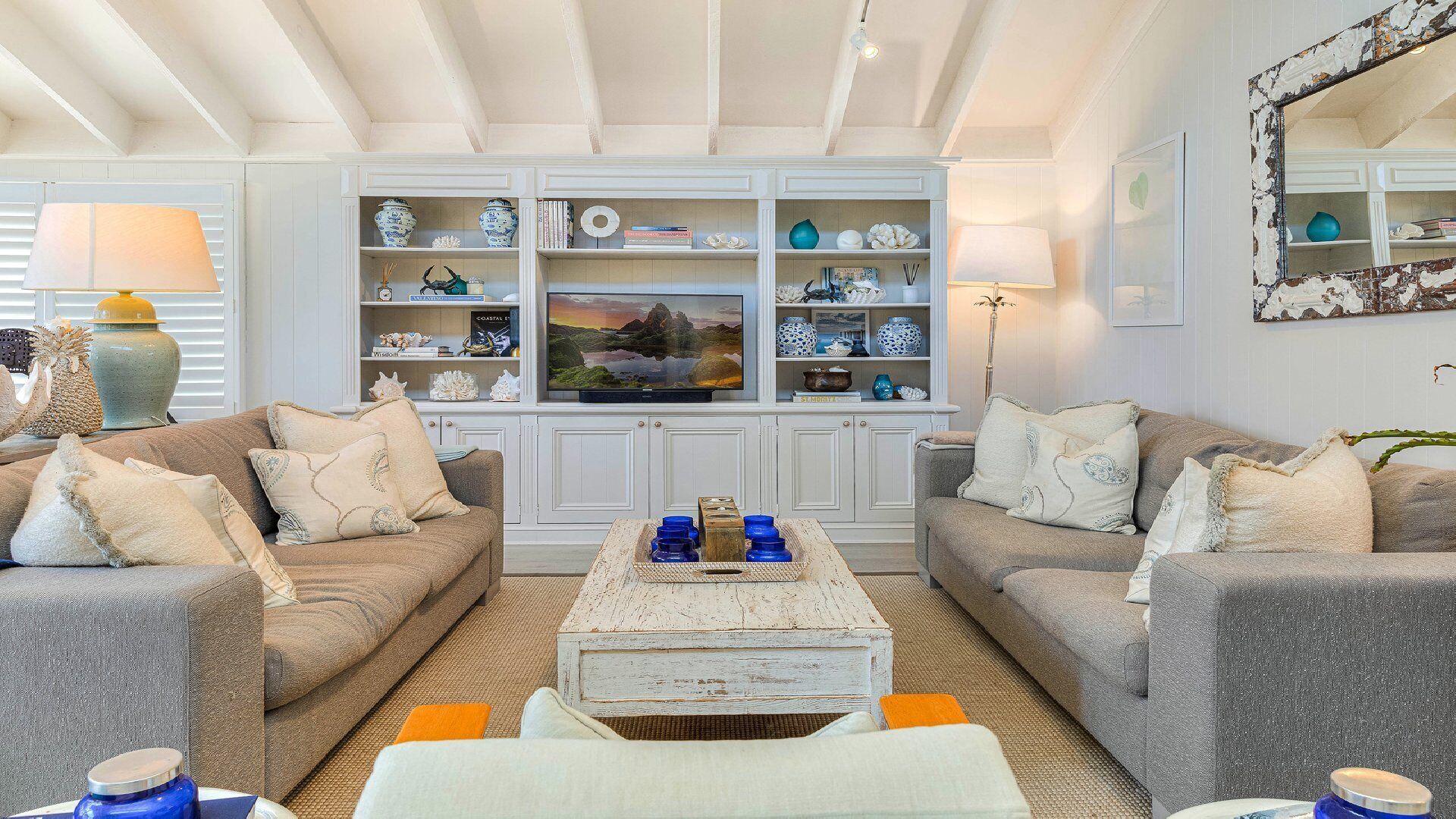Una sala de estar con dos sofás, una mesa de centro y un televisor. Hay estanterías con objetos decorativos y una lámpara.