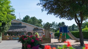 A café with a thatched roof, a playground with a slide, and a wooden fence with flowers.