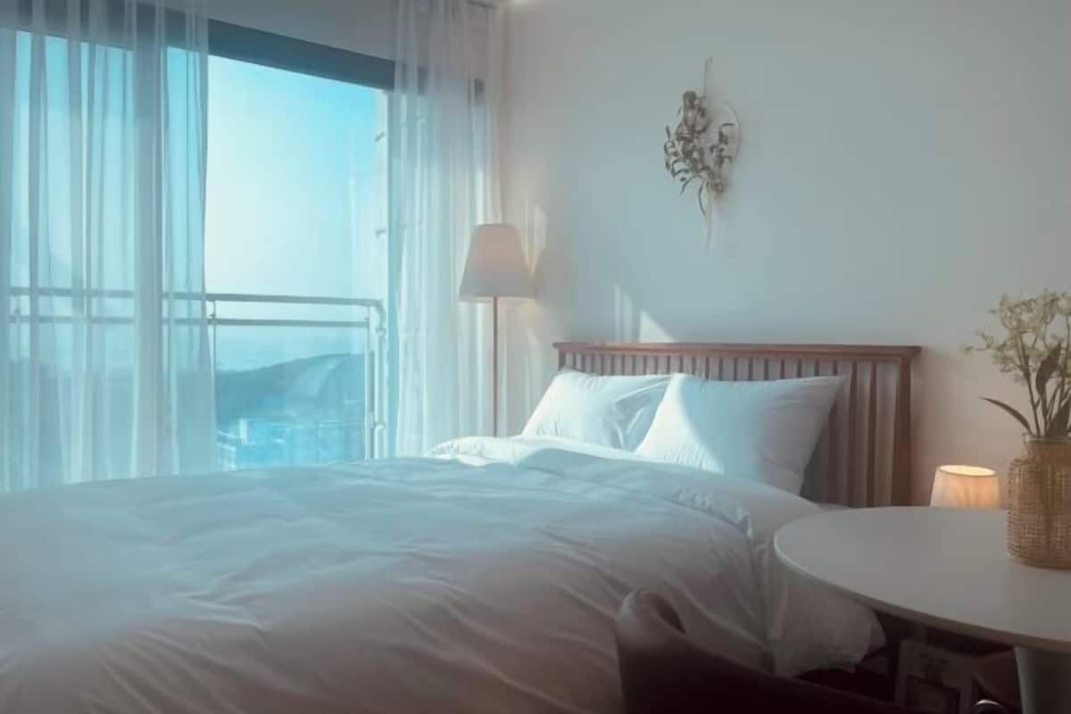 Une chambre d’hôtel avec un grand lit, une table ronde et une vue sur la mer, visible à travers de fines rideaux.