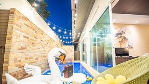 A modern outdoor pool area with a swan statue, a lounge chair, and a brick wall. - Aurora Life Pool Villa Pattaya (Pattaya)