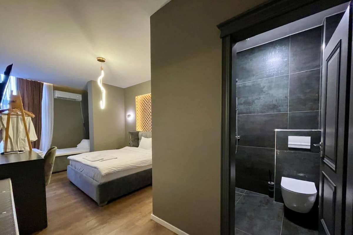 Ein modernes Hotelzimmer mit einem Bett, einem Schreibtisch und einem Badezimmer mit dunklen Fliesen.