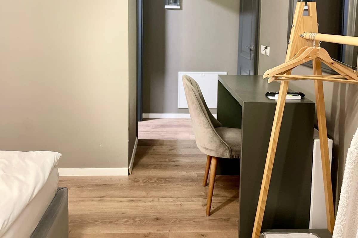 Ein Schlafzimmer mit einem Bett, einem Schreibtisch und einem Stuhl. Ein hölzernes Staffelei zeigt ein Gemälde, und ein weißes Handtuch liegt auf einem Tisch.