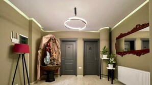 Un pasillo con una lámpara moderna, dos puertas con los números 103 y 102, una lámpara de pie roja y un espejo con un marco decorativo.