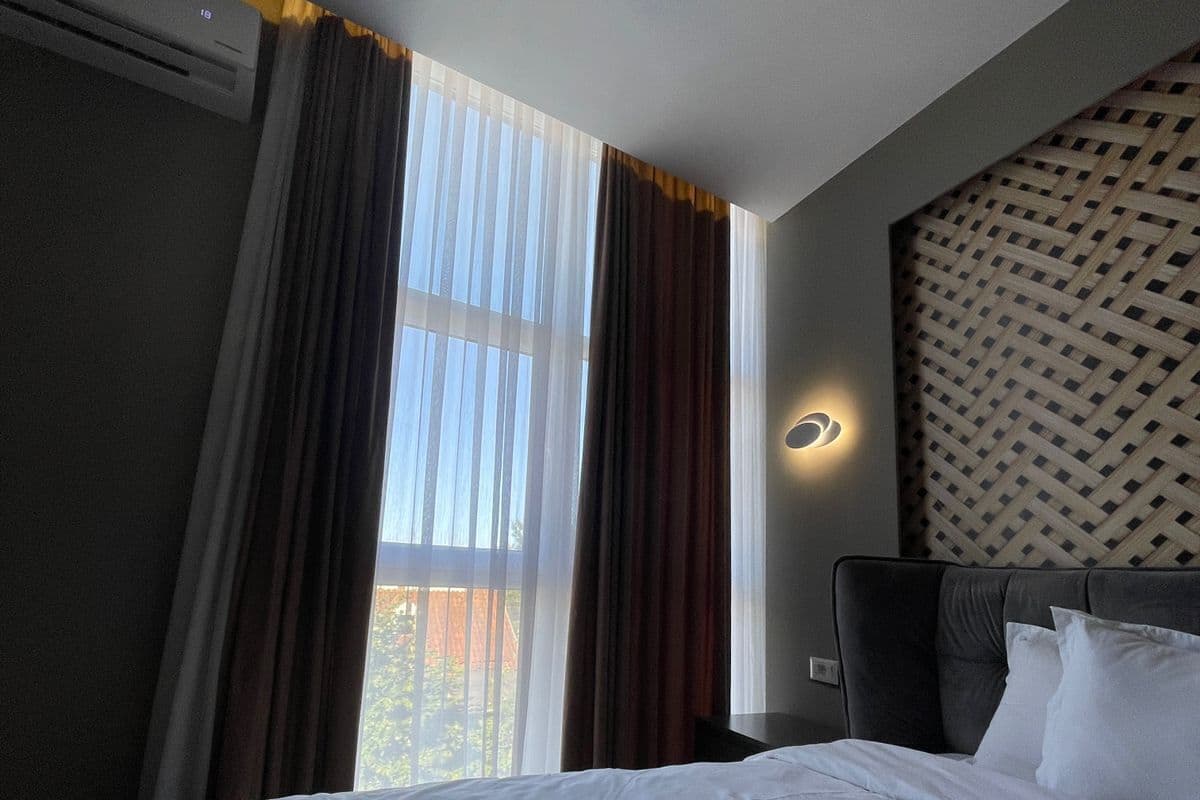 Ein Hotelzimmer mit Bett, Vorhängen, einer Wandleuchte und einer Wand mit Muster.