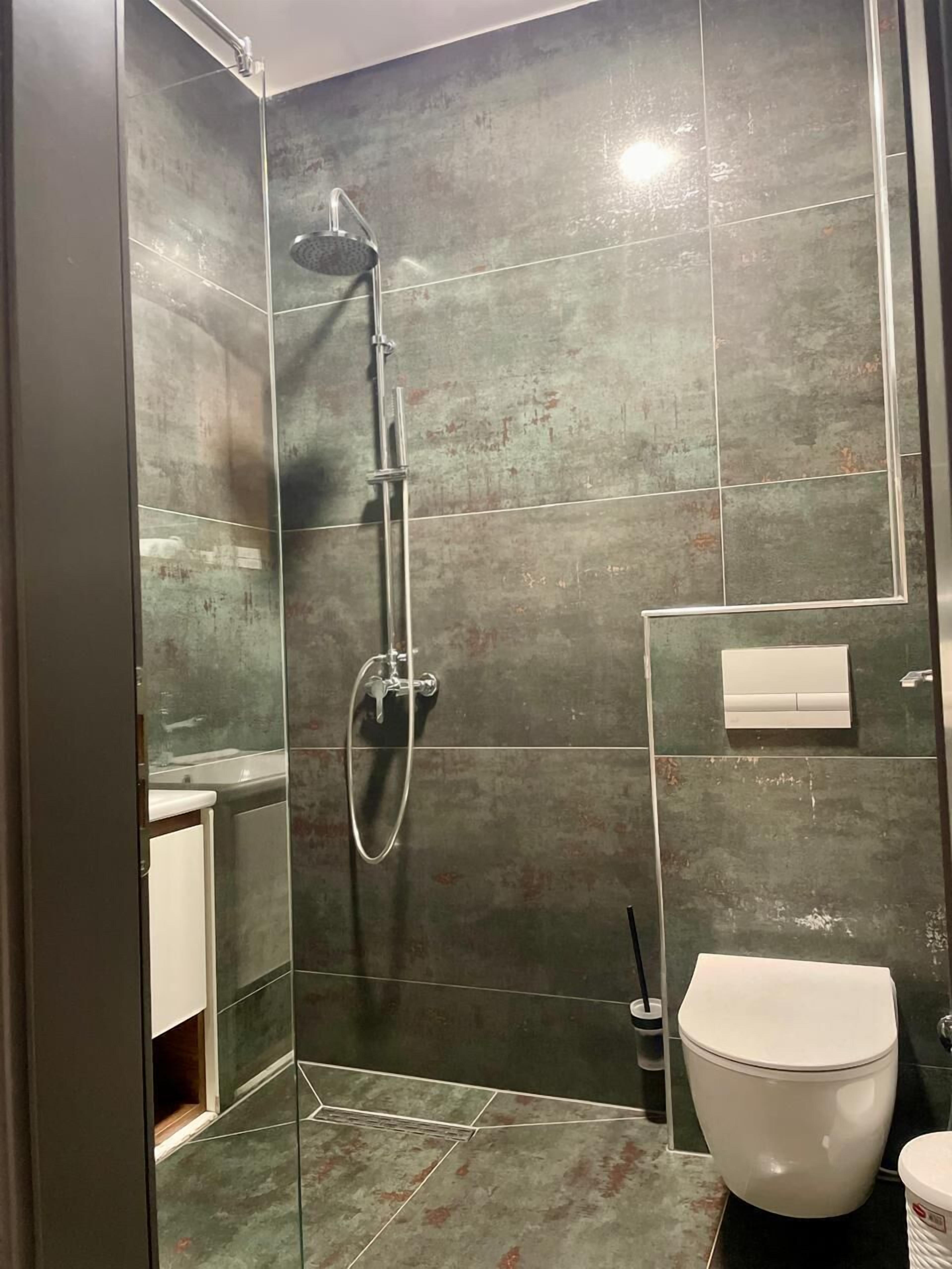 Un baño moderno con ducha envuelta en vidrio, un inodoro y un lavamanos pequeño.