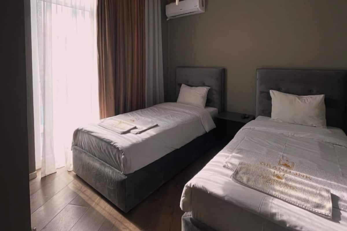 Ein Hotelzimmer mit zwei Betten, einem Deckenventilator, einer Klimaanlage und einem großen Fenster mit Vorhängen.