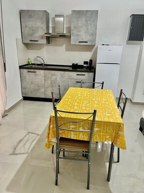 A compact kitchen with modern appliances, a dining table with chairs, and a yellow tablecloth. - Guesthouse the barber's store (Scalea)