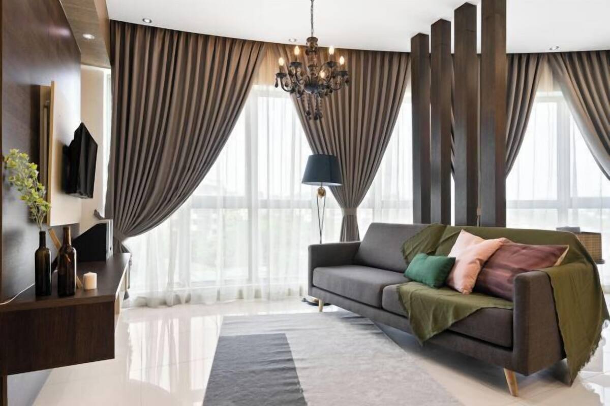 Ein modernes Wohnzimmer mit einer Couch, einer Kristallleuchter und großen Fenstern mit Vorhängen.