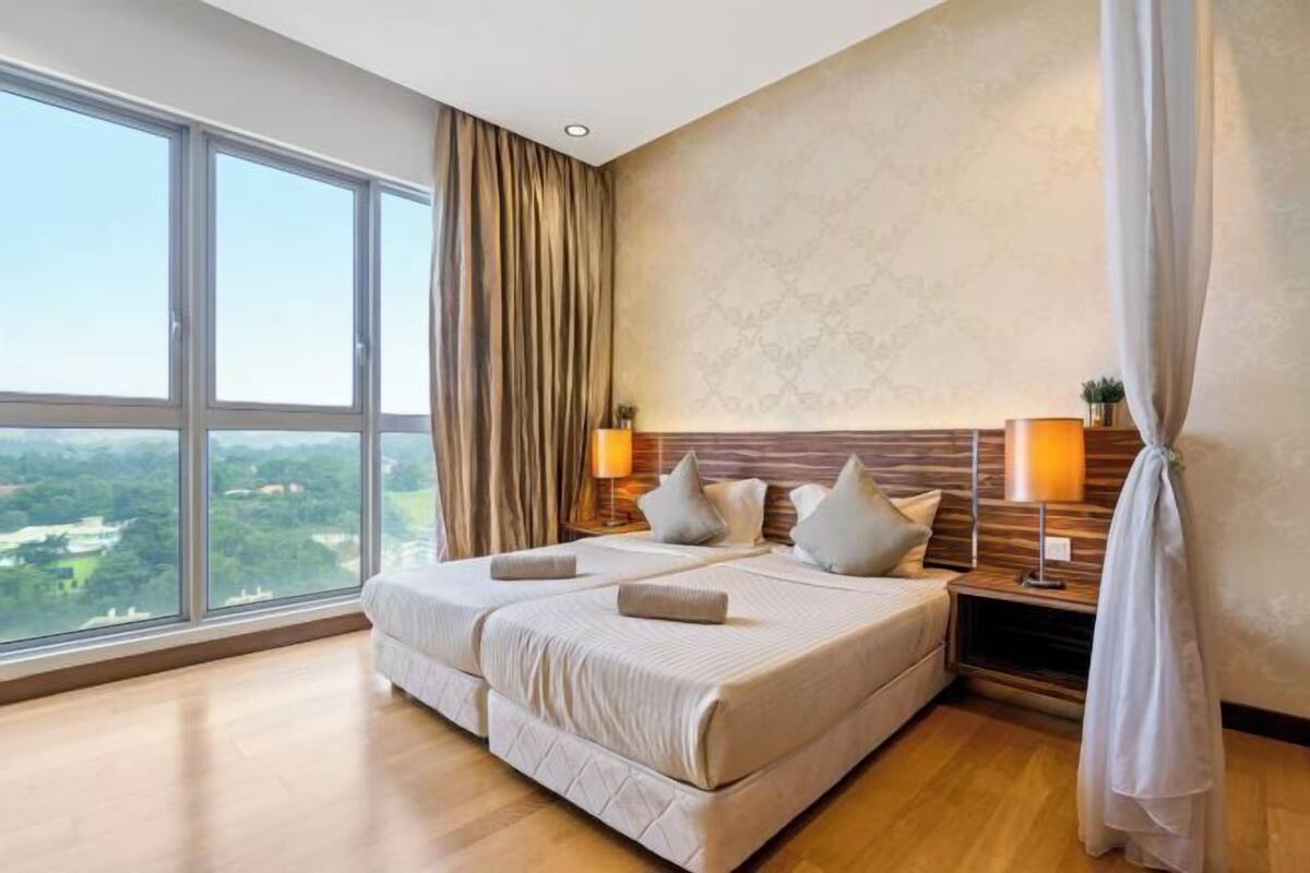 Ein großes Bett mit Blick auf eine Stadtansicht durch raumhohe Fenster, ein Holzkopfteil und zwei Nachttischlampen.
