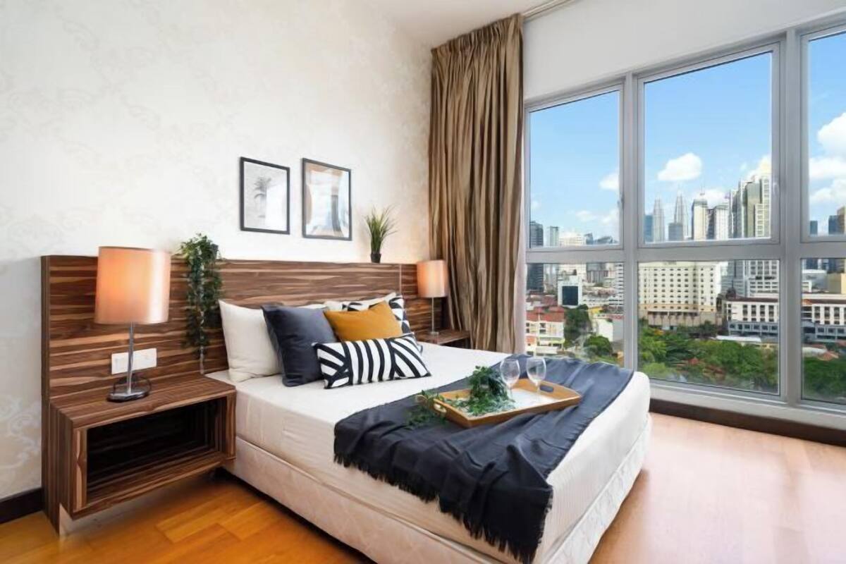 Ein modernes Hotelzimmer mit großem Fenster, einem Bett mit einem Tablett Gläser und Blick auf die Stadt.