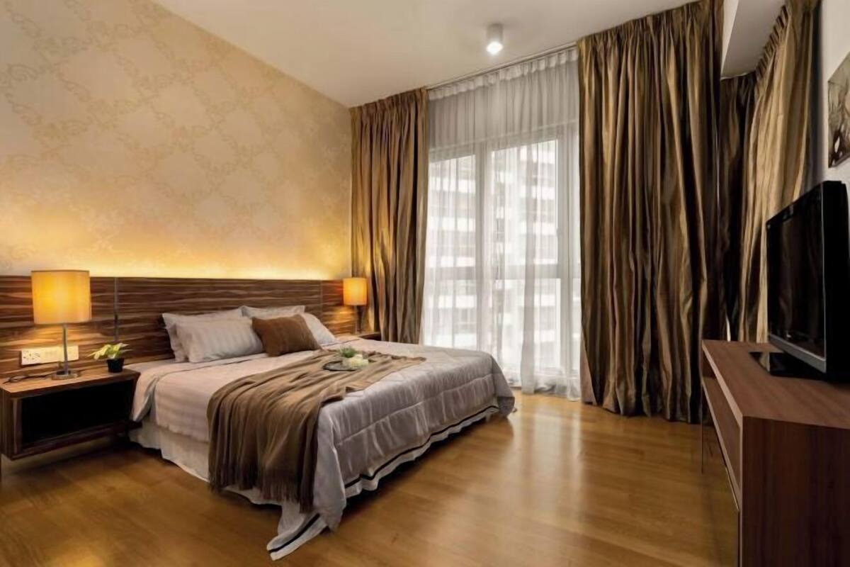 Ein Hotelzimmer mit einem großen Bett, einem hölzernen Kopfteil, zwei Nachttischlampen, einem Fernseher und einem Fenster mit Vorhängen.
