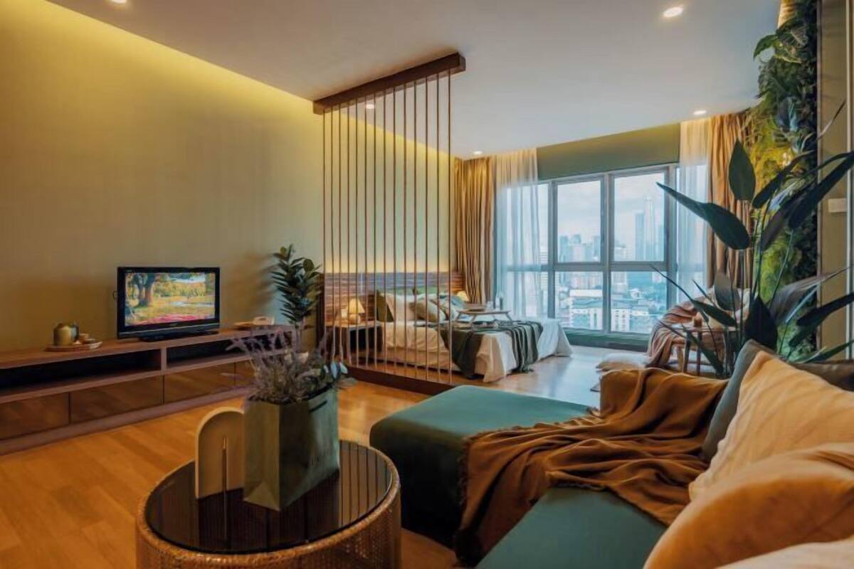 Ein modernes Wohnzimmer mit großem Fenster, Fernseher, Sofa und einer Zimmerpflanze.