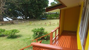 A wooden deck with a lattice railing, a yellow wall, and a view of a grassy yard with trees and a body of water in the background.