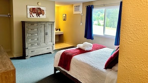 Une chambre à coucher avec un lit, une commode, une fenêtre avec des rideaux et une salle de bain visible au fond.