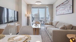 A hotel room with a dining area, a sofa, a TV, and a city view. - Vogue| Vida Dubai Mall with Direct ِAccess to Mall (Dubai)