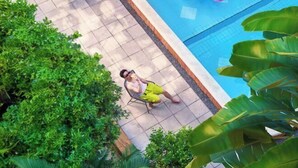Un homme est assis sur une chaise près d’une piscine, avec un flotteur rose en forme de cercle.