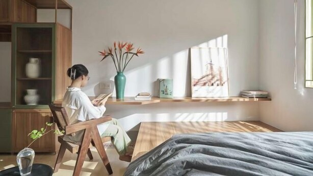 Une chambre moderne avec un lit, un fauteuil de lecture, une armoire en bois et une fenêtre laissant entrer la lumière naturelle.