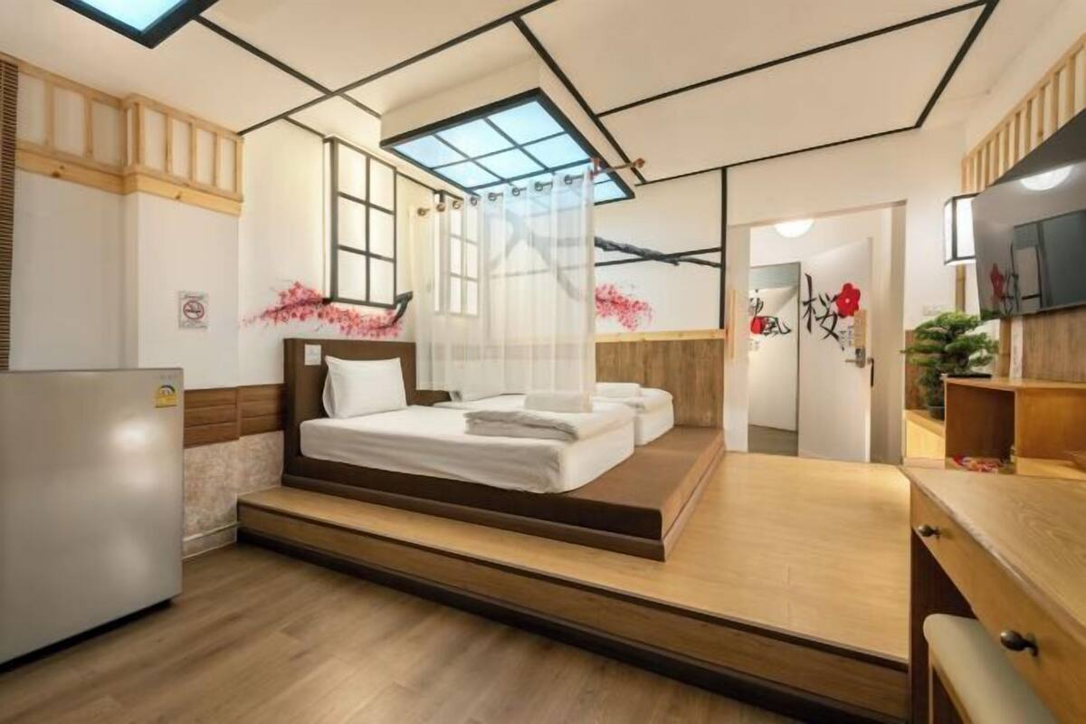 A bedroom with a bed, a desk, a chair, a refrigerator, and a skylight.
