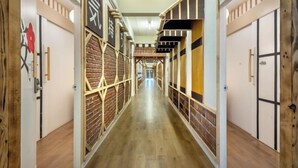 A corridor with wooden flooring, a brick wall on one side, and doors on the other. - Shibaroom Nakhonratchasima Central Korat (Nakhon Ratchasima)