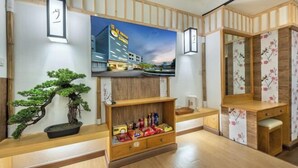 Ein traditioneller japanischer Raum mit Tatami-Böden, einer Bonsai-Pflanze, einem Holzschrank mit Snacks, einem an der Wand montierten Fernseher und einem Holzschrank mit Spiegel.