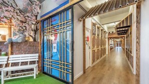 A hotel corridor with a wooden floor, a bench, and a door with a blue and white design. - Shibaroom Nakhonratchasima Central Korat (Nakhon Ratchasima)