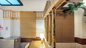 Ein Zimmer mit einem Holztisch, einer Lampe, einem Kühlschrank und Bambus-Elementen.
