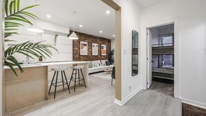 Una cocina moderna con encimera blanca, taburetes de bar y una pared decorada con ladrillos.