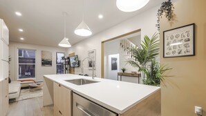 Una cocina moderna con una isla central, electrodomésticos de acero inoxidable, iluminación colgante y vista al área de estar.