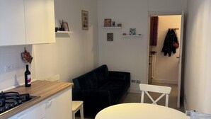 A modern kitchen with white cabinets, a wooden countertop, a gas stove, and a hanging pendant light. There is a black sofa and a white dining table with chairs in the living area. - Casetta Martesana - new one-bedroom apartment on the naviglio (Milano)