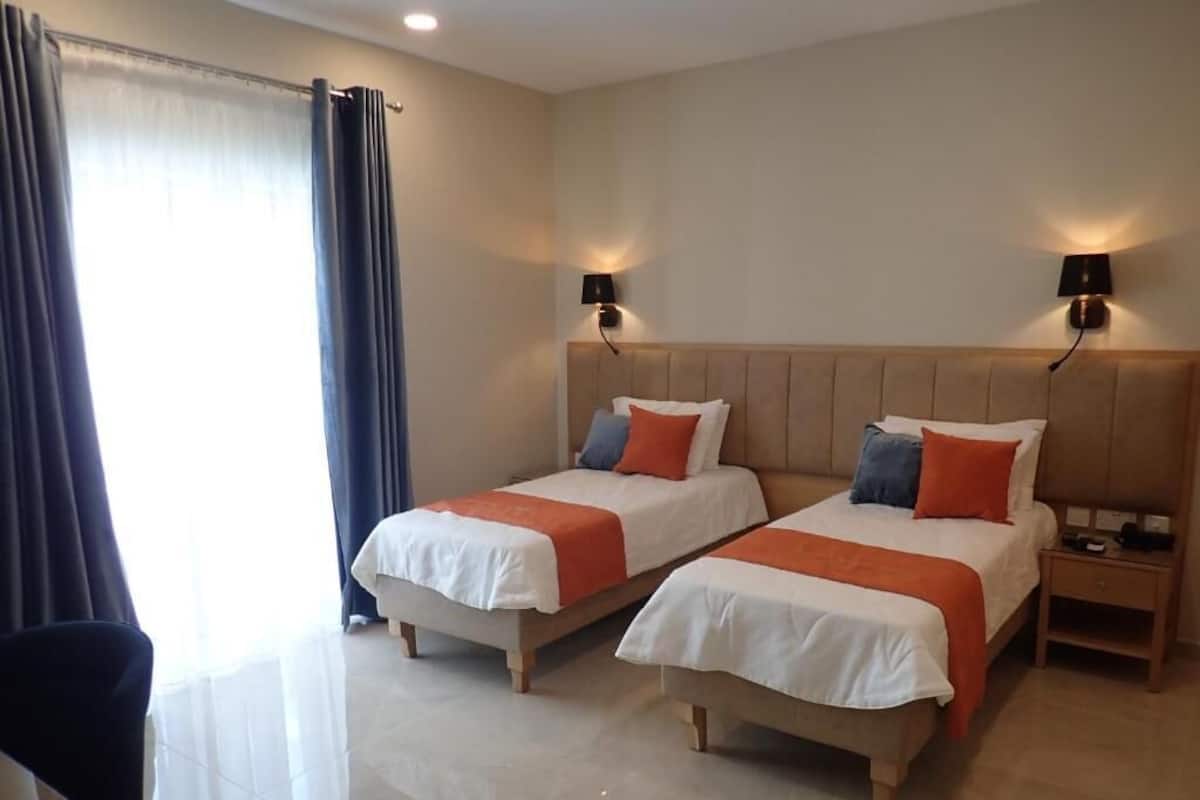 A hotel room with two beds, a nightstand, a chair, and a window with curtains.