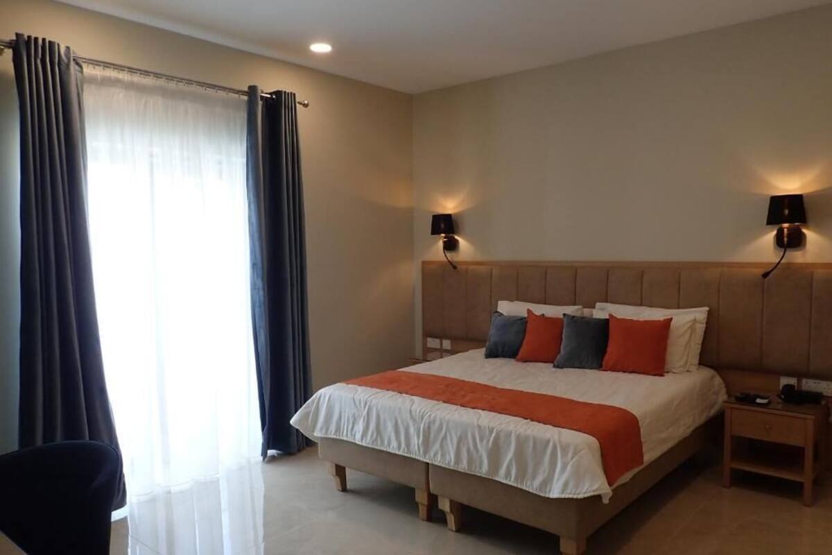 A hotel room with a large bed, two bedside lamps, a nightstand, a chair, and a window with curtains.