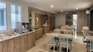 A modern kitchen with a wooden counter, a coffee machine, and a dining area with white chairs and blue cushions. - Duncan guest house (Marsaxlokk)