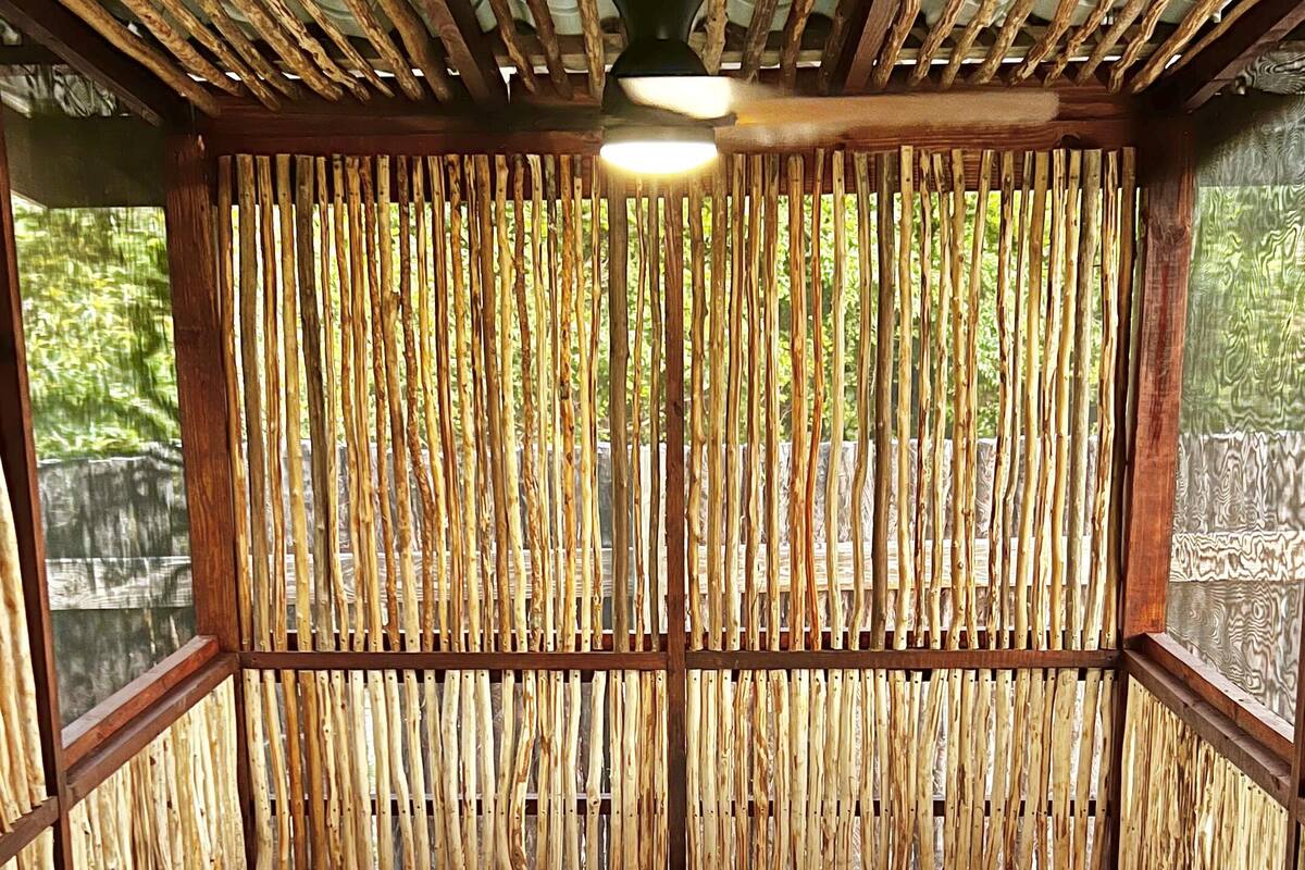 A hot tub with a control panel, surrounded by a bamboo wall, and a basket with a bottle and glass on the edge.