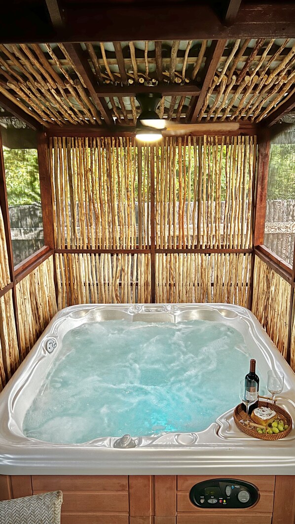 A hot tub with a control panel, surrounded by a bamboo wall, and a basket with a bottle and glass on the edge. - Kmar Villas (Maya Beach)