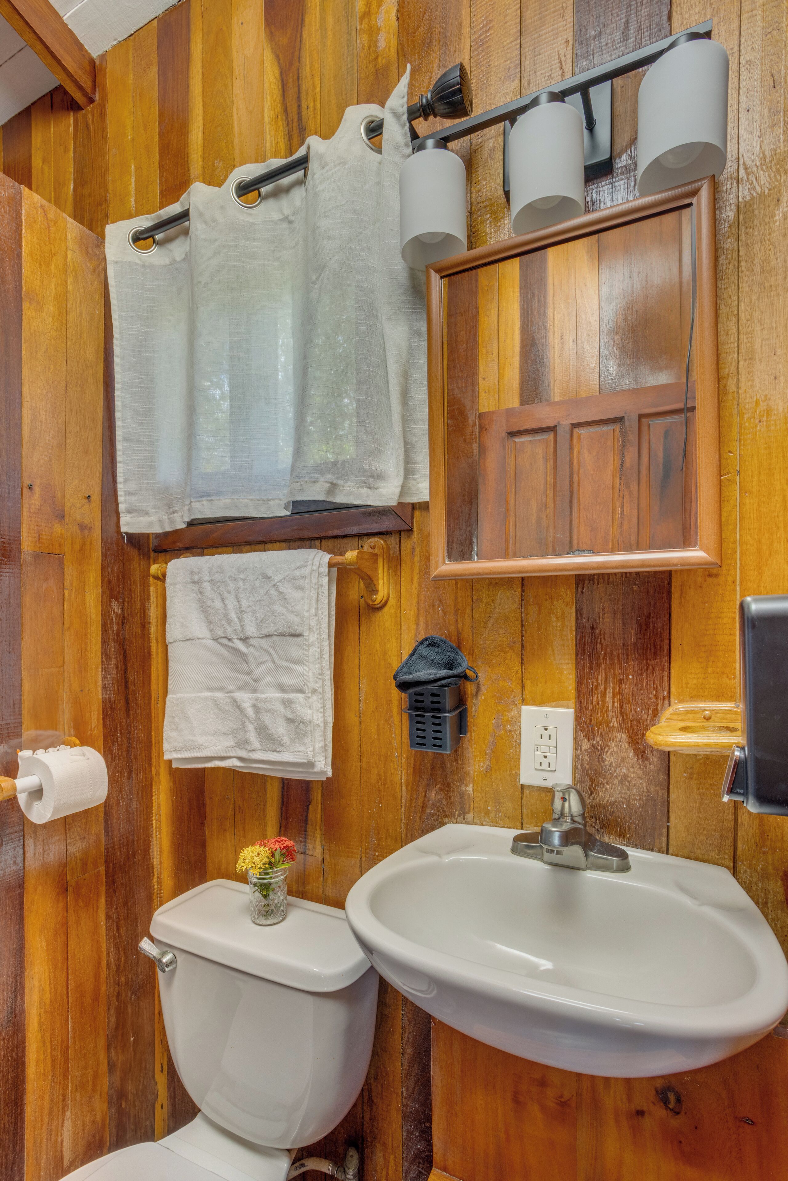 Un bagno con rivestimenti in legno, dotato di WC, lavandino, porta asciugamani e specchio.