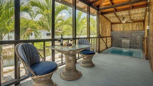 A covered outdoor area with a glass table and wicker chairs, overlooking a swimming pool and lush greenery. - Kmar Villas (Maya Beach)